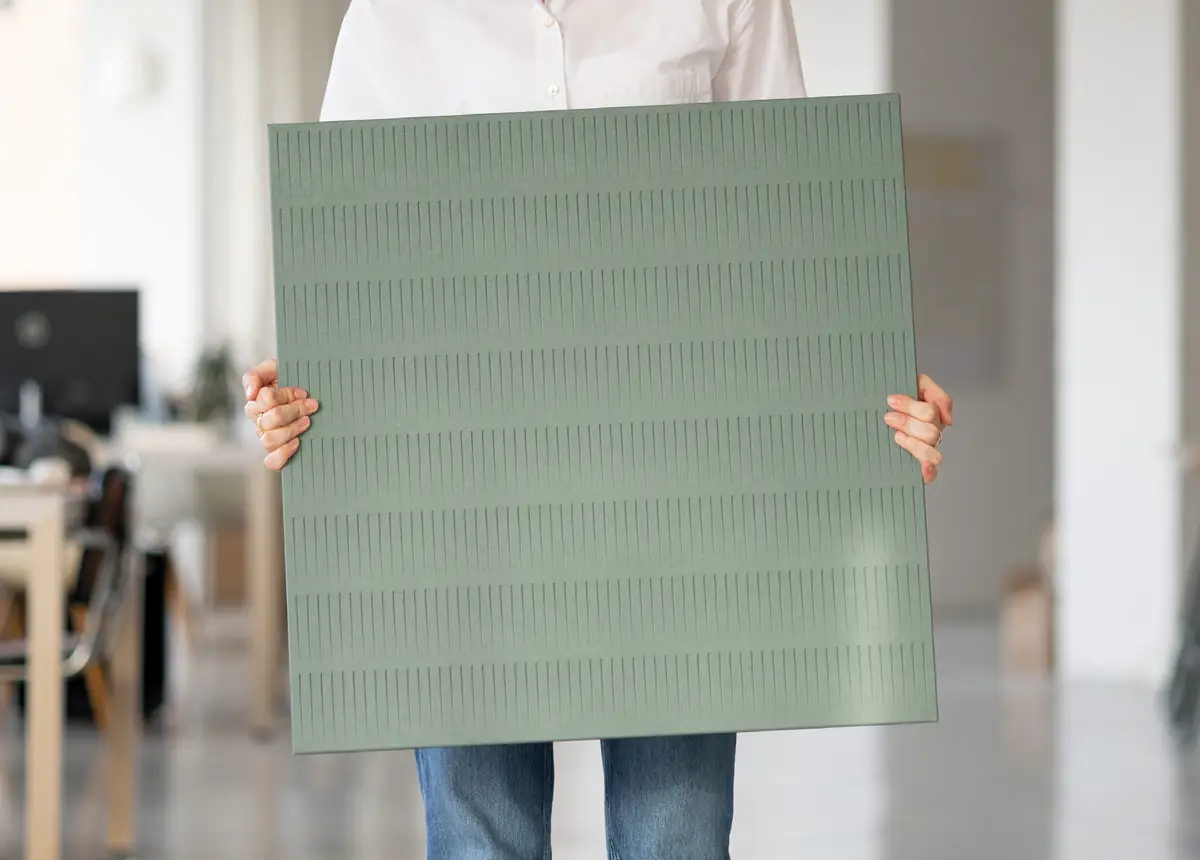 Persona sosteniendo un panel cuadrado verde con relieve en una oficina