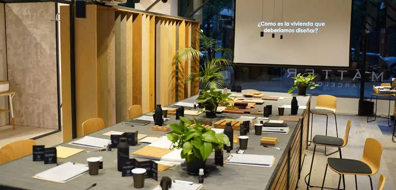 Mesa de materiales de Matter Barcelona preparada para el encuentro, con la pregunta «¿Cómo es la vivienda que deberíamos diseñar?» proyectada en la pantalla.