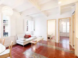 Salón luminoso con suelo de baldosa roja tradicional, sofá blanco y techo de vigas pintadas de blanco.