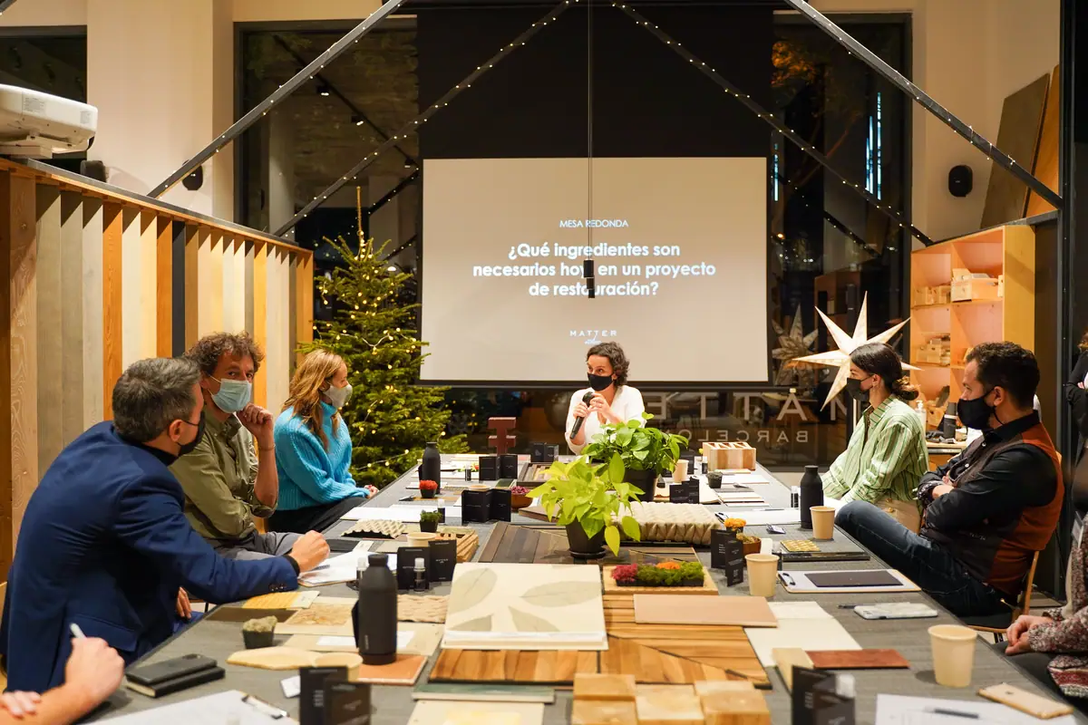 Ponentes y asistentes sentados alrededor de la mesa de materiales de Matter Barcelona, con una pantalla que plantea la pregunta de la mesa redonda