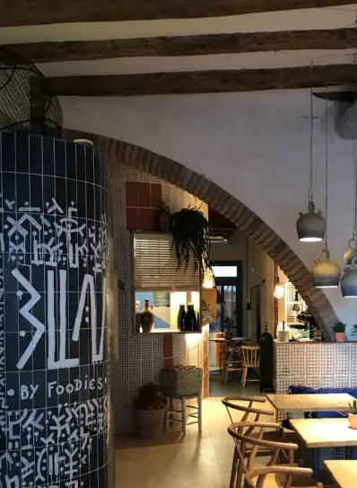 Interior del restaurante Blau con una columna revestida de azulejo azul con el rótulo, un arco de ladrillo y vigas de madera