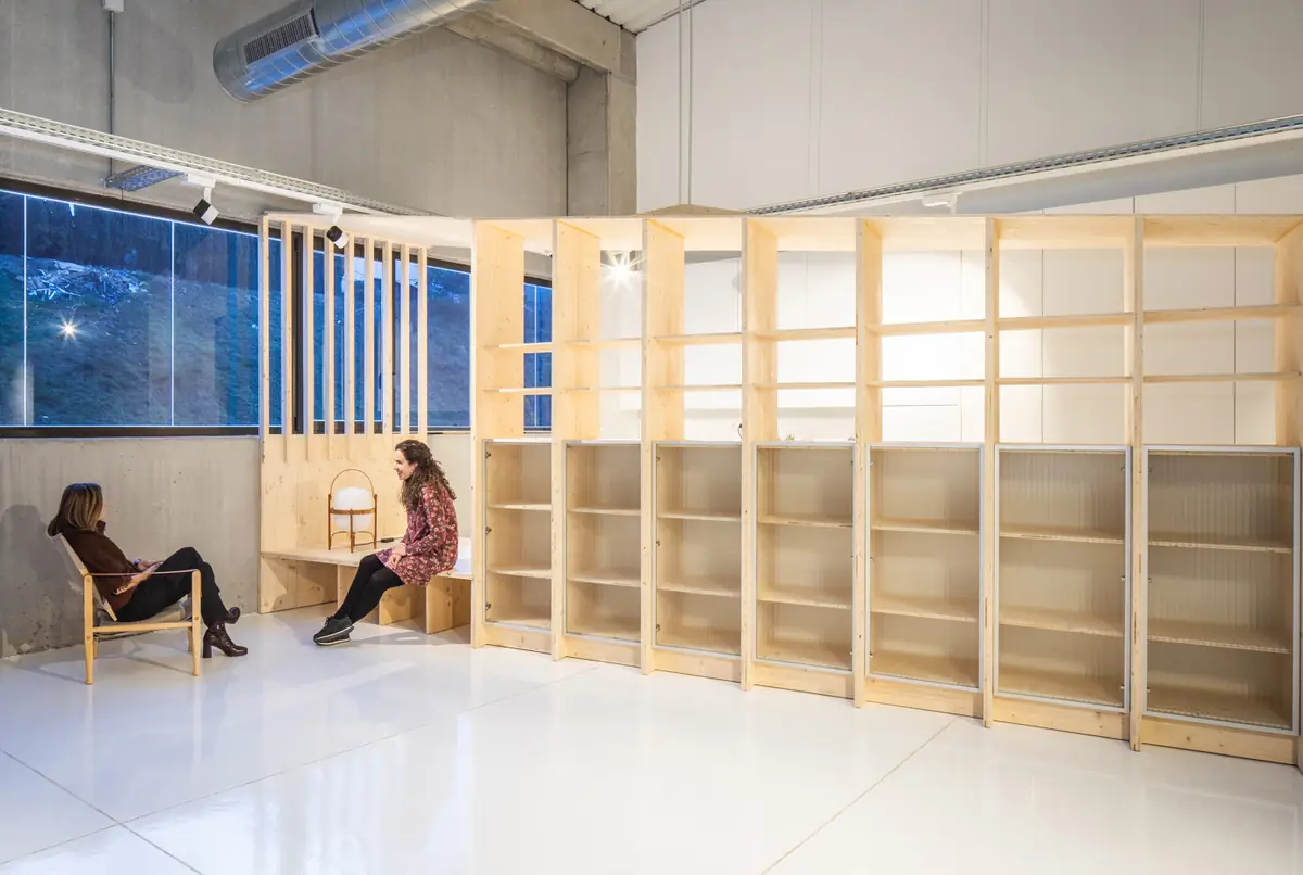 Mueble de estanterías de madera clara con un rincón de descanso en una nave de paredes blancas