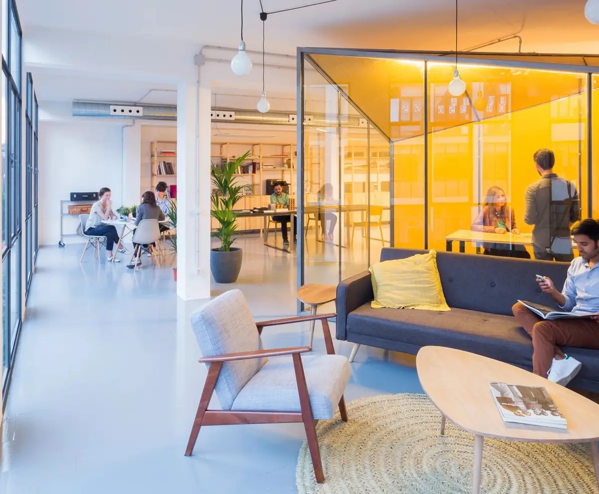 Oficina luminosa con sofá azul, butaca y una sala acristalada de interior amarillo al fondo