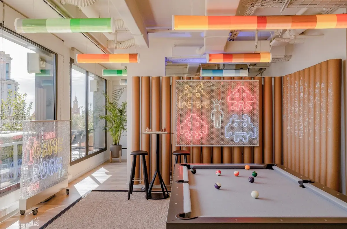 Sala con mesa de billar, neones de marcianitos en la pared y tubos de colores en el techo