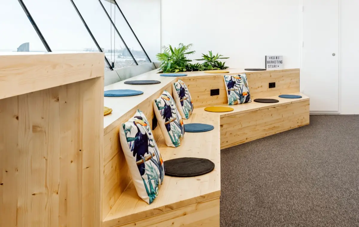 Banco corrido de madera clara con cojines estampados y plantas bajo una ventana inclinada