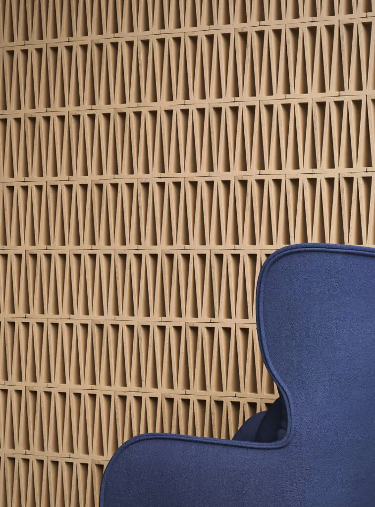 Pared de piezas de terracota Celosia con motivo triangular repetido tras un sillón azul