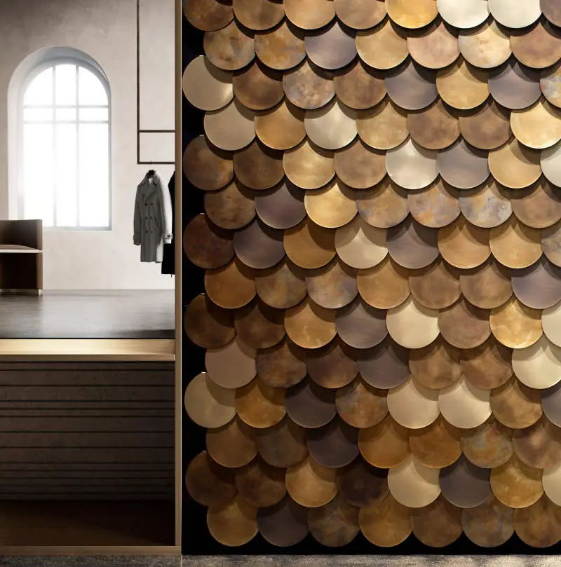 Pared revestida con discos metálicos superpuestos en tonos dorados, bronce y marrón
