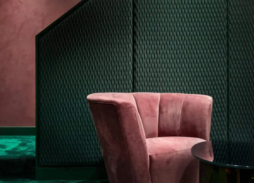 Sillón de terciopelo rosa ante una pared revestida con paneles textiles verdes en relieve