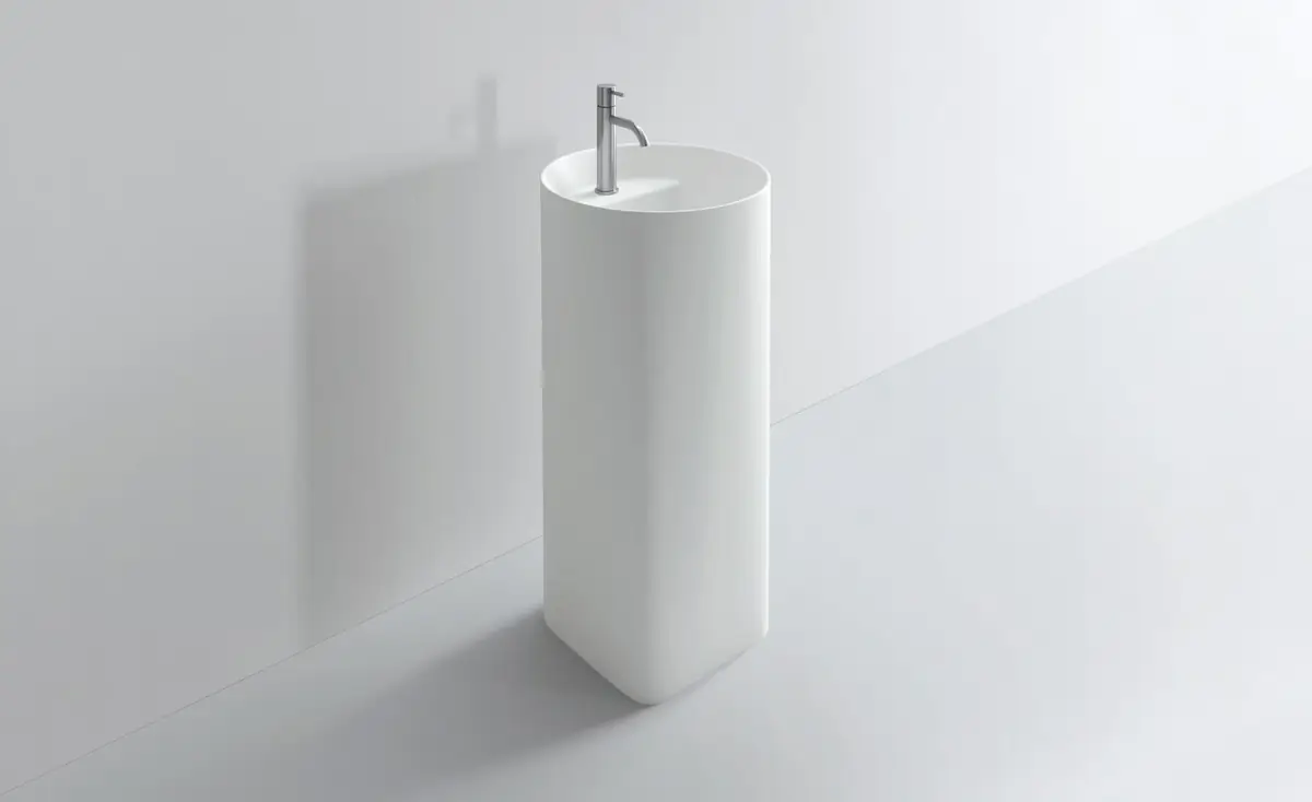 Lavabo de pie blanco de sección circular con grifo alto, sobre fondo gris claro.