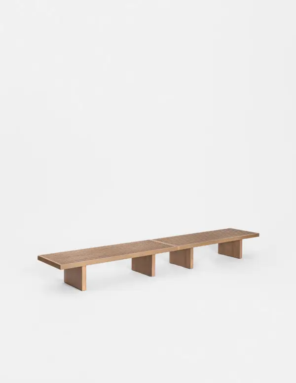 Banco bajo de listones de madera clara apoyado sobre tres soportes macizos.