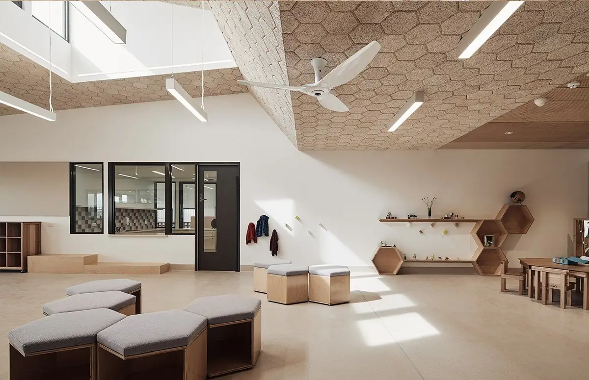 Sala amplia con techo inclinado revestido de baldosas hexagonales de lana de madera, lucernario y asientos hexagonales