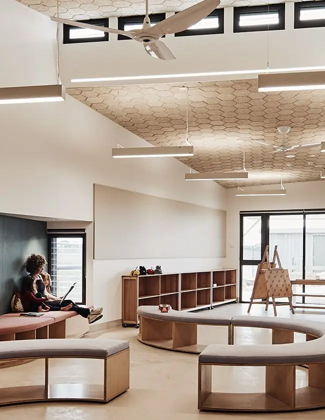 Sala con bancos curvos y estanterías de madera bajo un techo inclinado de baldosas hexagonales