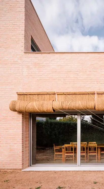 Fachada de ladrillo de la casa MS5 con una gran cristalera y un toldo de fibra trenzada