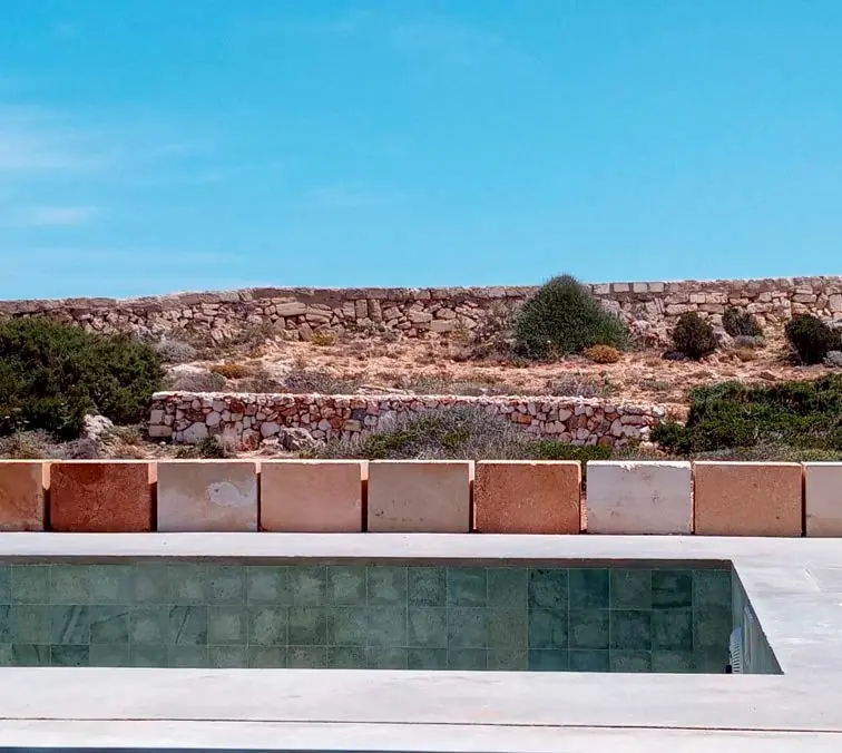 Piscina de la vivienda CP37 con muros de piedra seca y vegetación menorquina al fondo