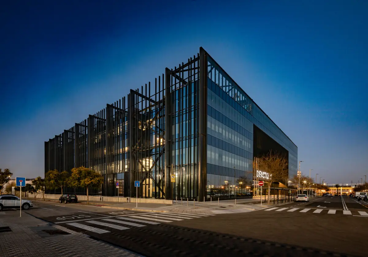 Edificio DFactory de vidrio con una estructura exterior de lamas verticales oscuras al anochecer
