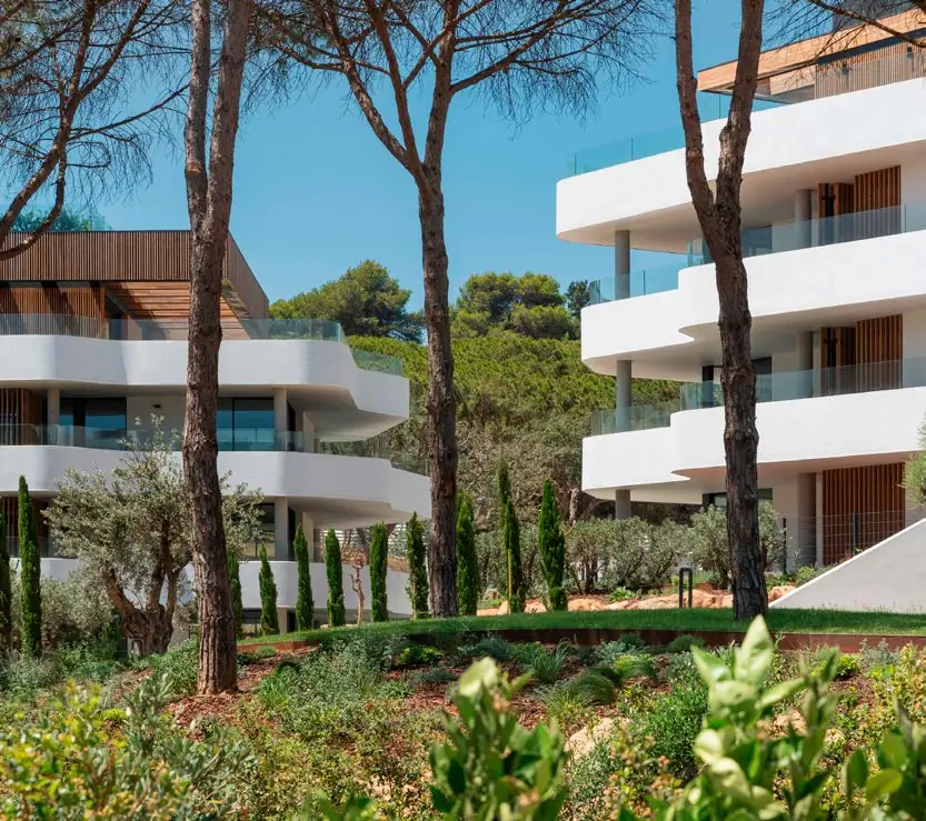 Edificios residenciales blancos con terrazas ajardinadas entre pinos y vegetación mediterránea