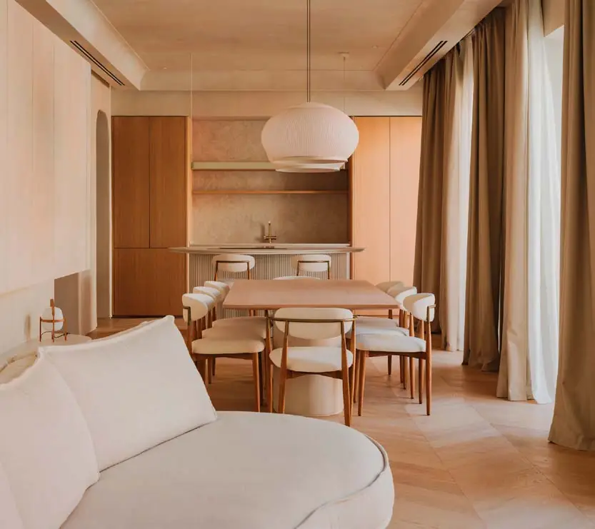 Salón y comedor con paredes claras de microcemento, suelo de roble y sofá curvo
