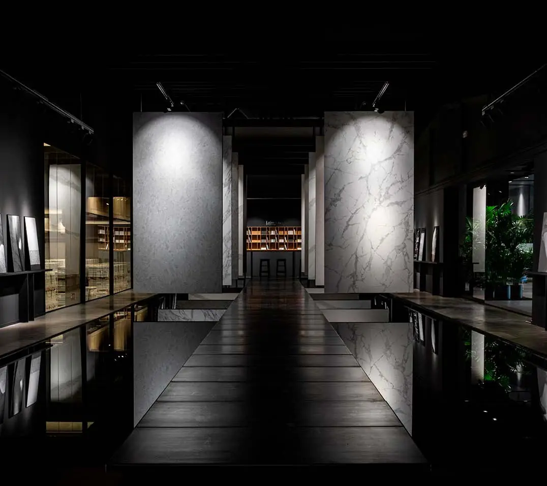 Showroom oscuro con grandes losas de piedra sinterizada suspendidas sobre un pavimento reflectante