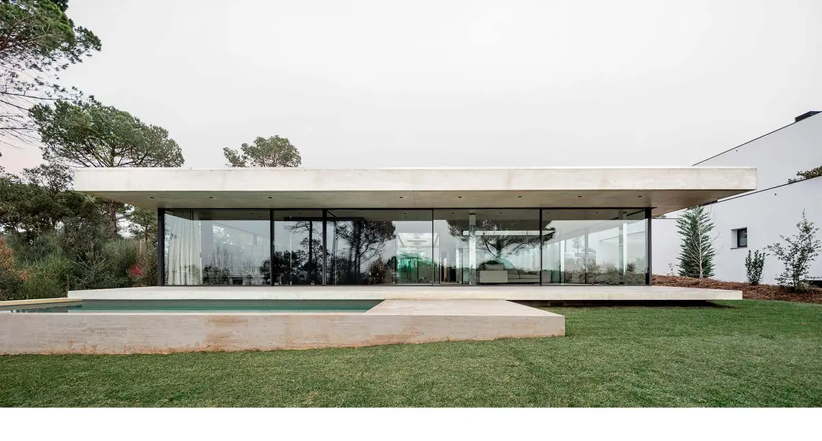 Vivienda horizontal bajo una losa de hormigón con fachada de vidrio frente a un jardín