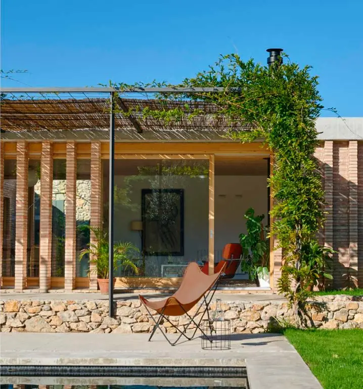 Porche con pérgola vegetal, celosía de ladrillo y una butaca junto al jardín