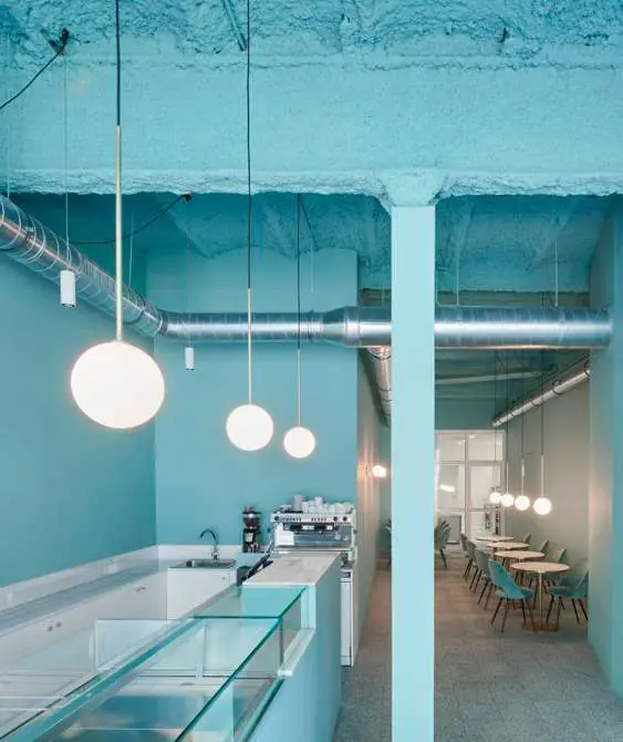 Pastelería Plume: espacio monocolor turquesa con techo de aislante proyectado y lámparas de globo