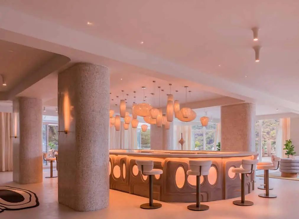 Bar circular con taburetes y lámparas de papel suspendidas en un interior blanco con pilares redondos