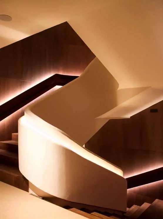 Escalera escultórica de formas curvas en tono claro con iluminación lineal cálida