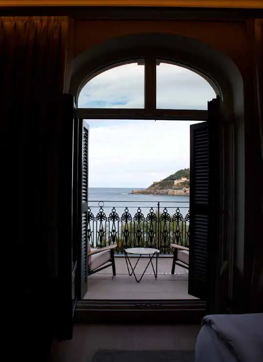 Ventana en arco abierta a un balcón con barandilla de forja y vistas al mar