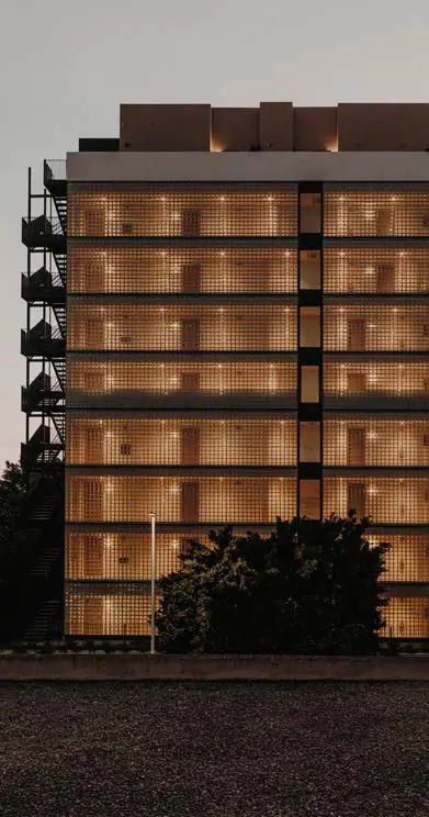 Fachada del hotel con celosías de pavés iluminadas desde el interior al anochecer