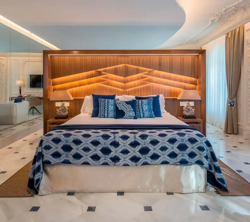 Dormitorio con cabecero de madera iluminado y colcha estampada en azul