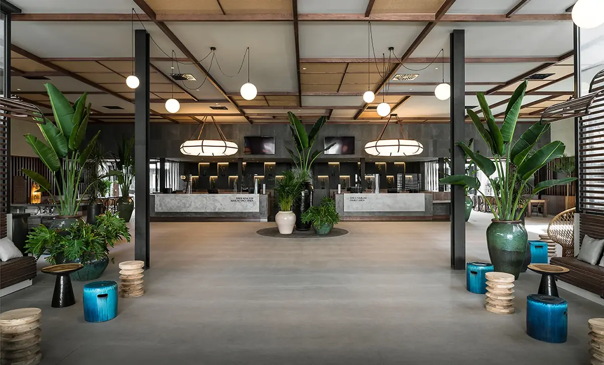 Lobby amplio con techo de madera, grandes plantas en macetas cerámicas y taburetes azules