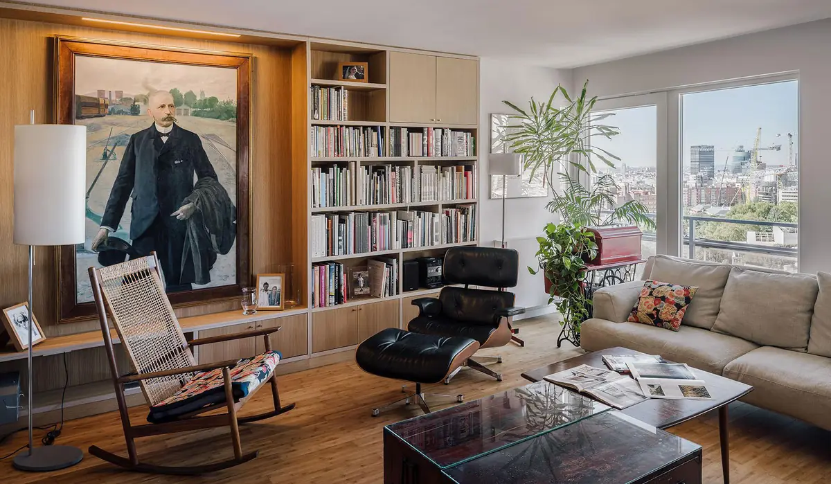 Salón con librería de madera a medida, butaca de cuero negro, mecedora y ventanales sobre la ciudad