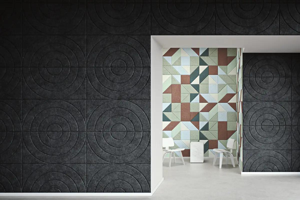Pared de baldosas de lana de madera gris oscuro con relieves circulares concéntricos y, al fondo, una pared de triángulos en verdes, azules y teja
