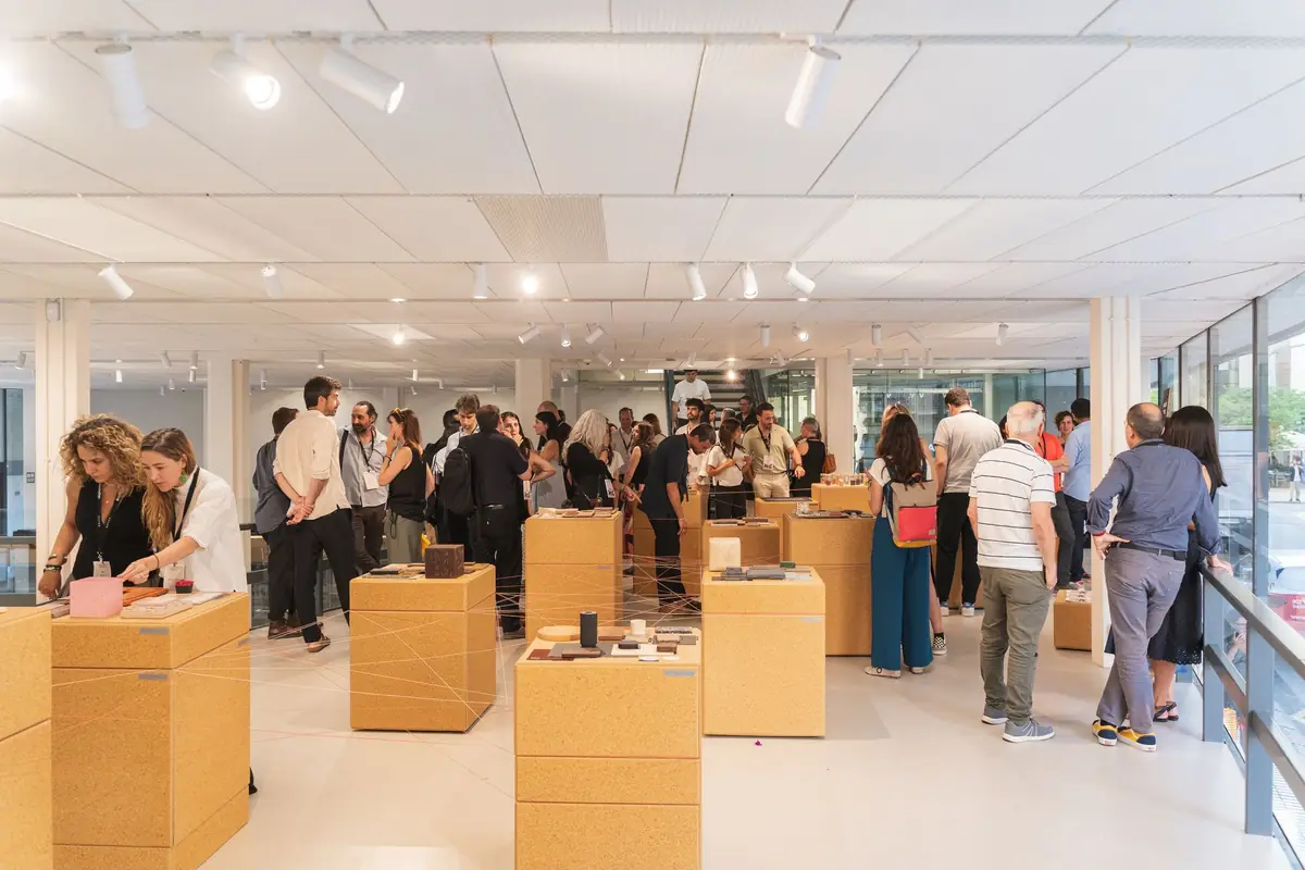 Vista general de la exposición con tótems de tablero de cascarilla de arroz y visitantes en el Altillo del COAC