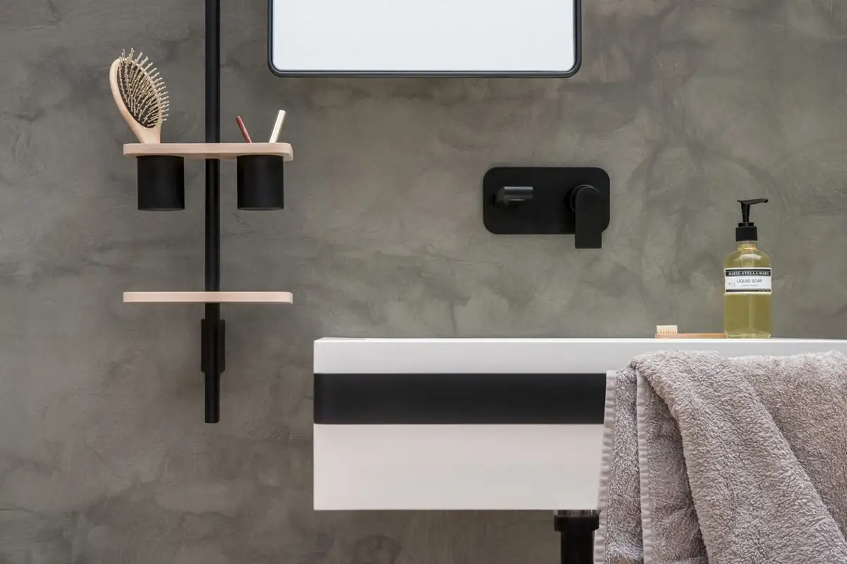 Barra vertical negra con estantes de madera y vasos negros junto a un lavabo y una grifería mural negra