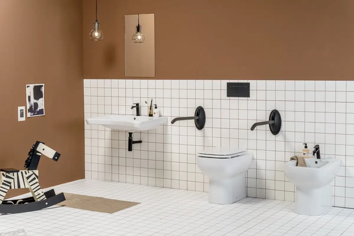 Baño con alicatado blanco y pared marrón, lavabo, inodoro y bidé con barras abatibles negras en la pared