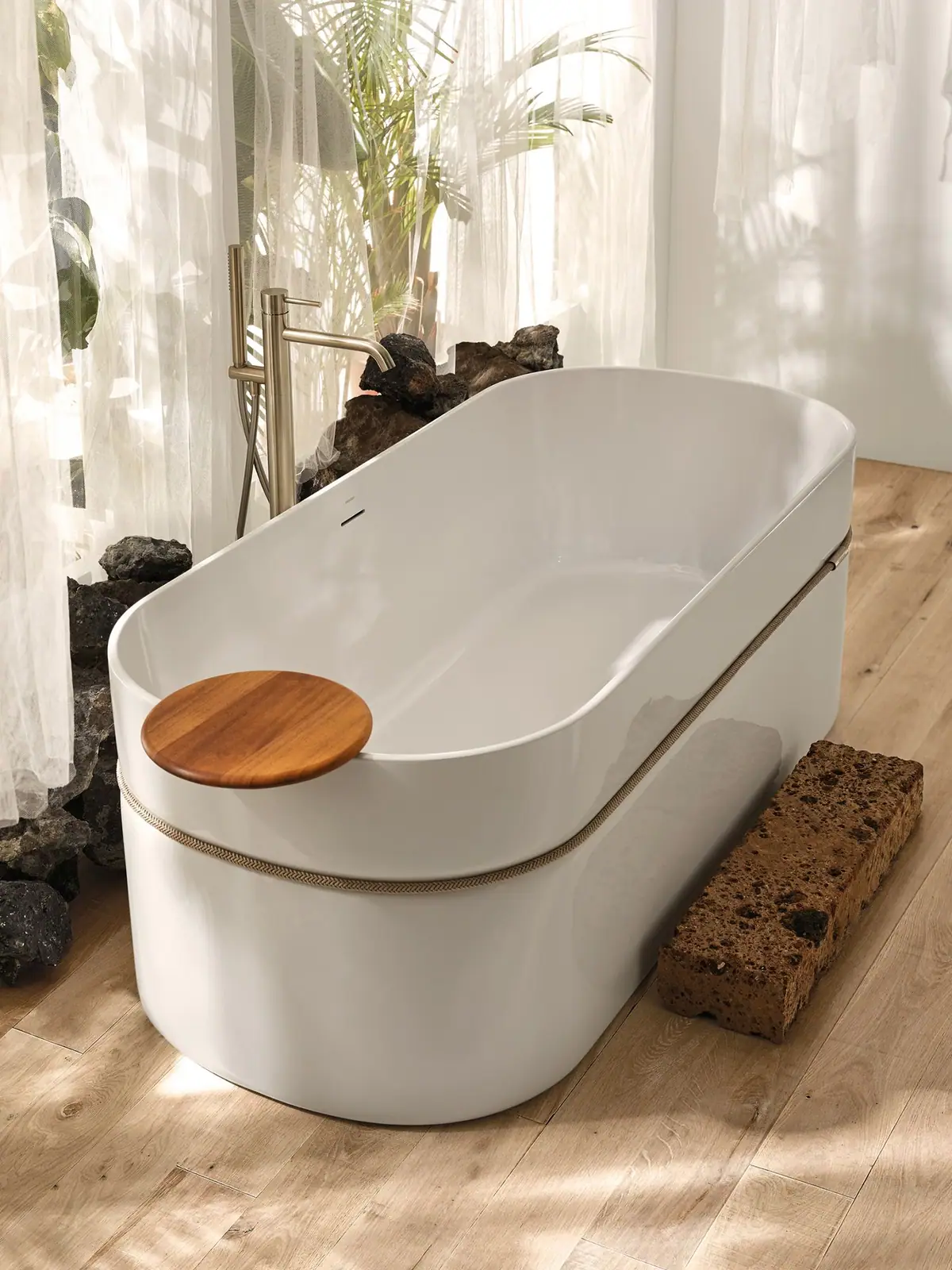 Bañera Tempo blanca con cuerda beige alrededor y una bandeja redonda de madera sobre el borde, junto a una grifería exenta