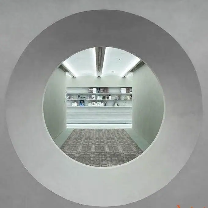 Abertura circular en un muro revestido de cemento decorativo gris que enmarca una sala de exposición