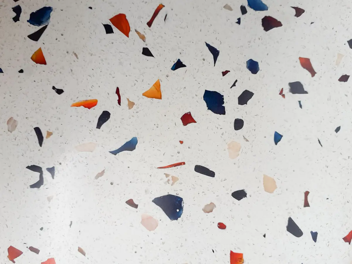 Superficie blanca de microterrazo con fragmentos de vidrio de colores azul, rojo, naranja y gris