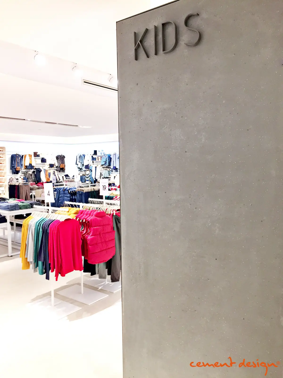Volumen revestido de cemento con efecto de hormigón visto y la palabra KIDS en una tienda de moda