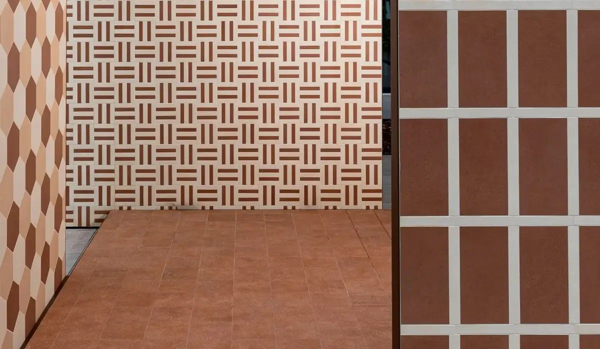 Paredes con composiciones geométricas de piezas cerámicas en tonos crema y terracota y suelo de color ladrillo.