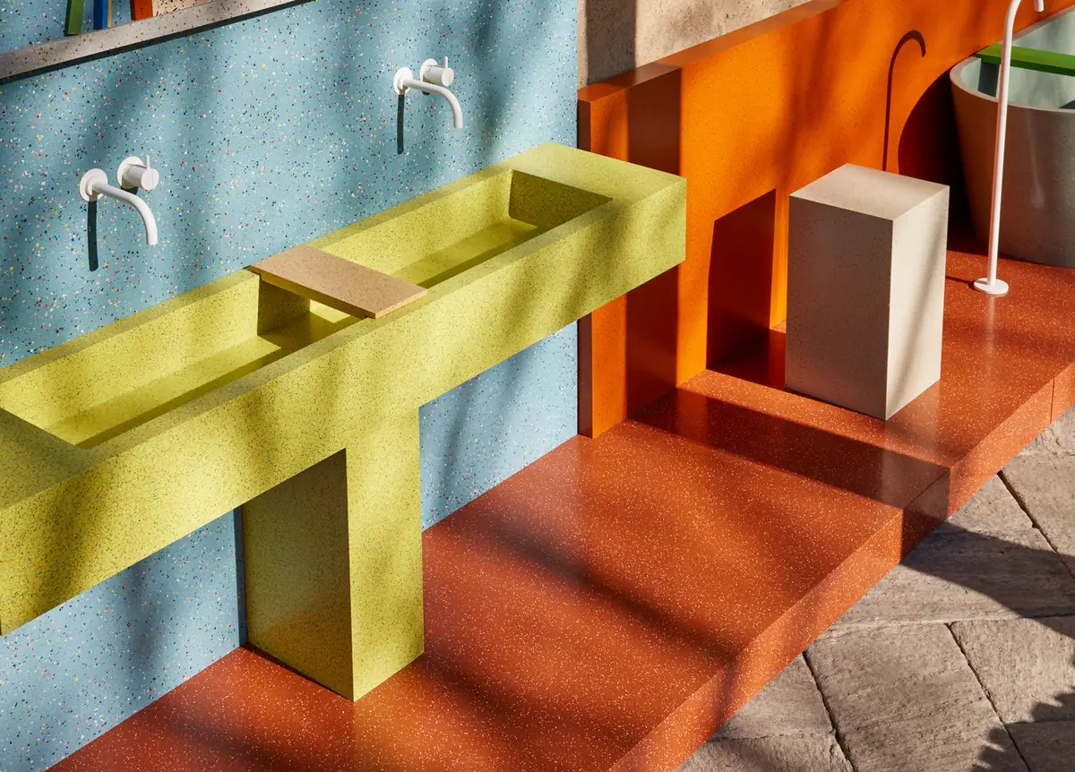 Lavabo corrido verde lima ante una pared azul moteada y sobre una plataforma color teja, todo en superficie sólida