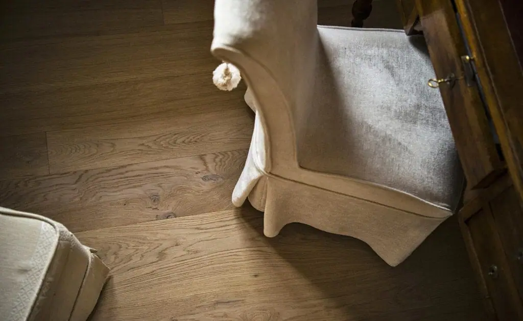 Butaca tapizada en blanco junto a un mueble de madera sobre un suelo de tablas de roble de tono miel con nudos