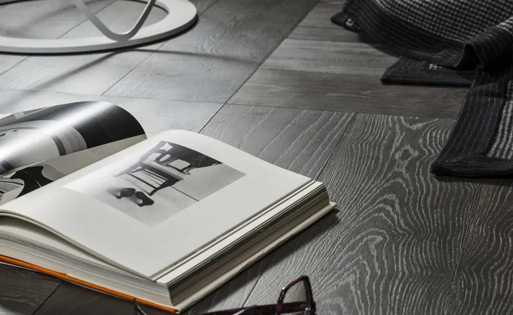Libro abierto y una manta sobre un suelo de tablas de roble en tono gris oscuro con la veta realzada en claro
