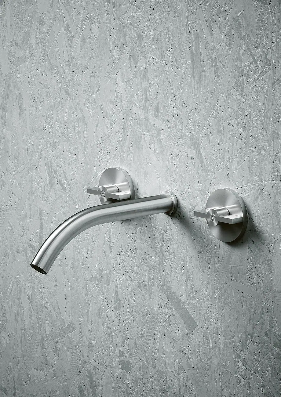 Caño de pared curvo de acero entre dos mandos circulares sobre una pared gris con textura