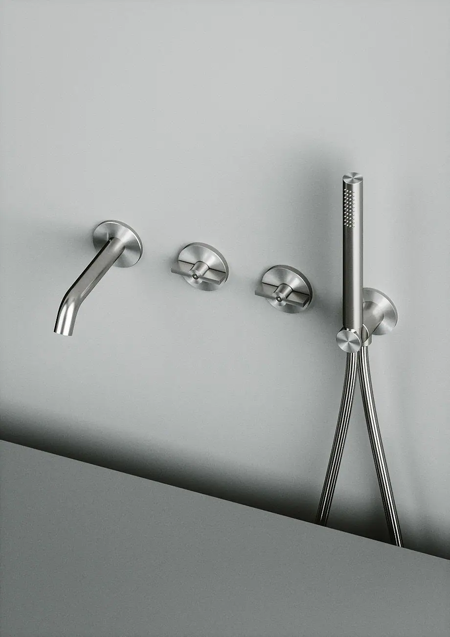 Caño de pared, dos mandos circulares y ducha de mano con soporte de acero sobre una pared gris