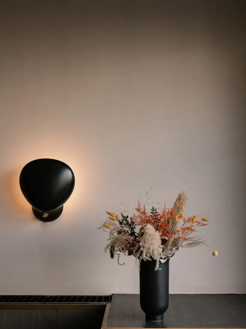 Aplique negro encendido y jarrón con flores secas sobre una pared lisa de yeso mineral