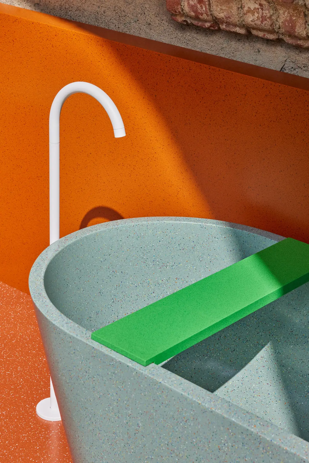 Bañera exenta de superficie sólida verde agua con una tabla verde y un grifo blanco de pie, ante una pared naranja