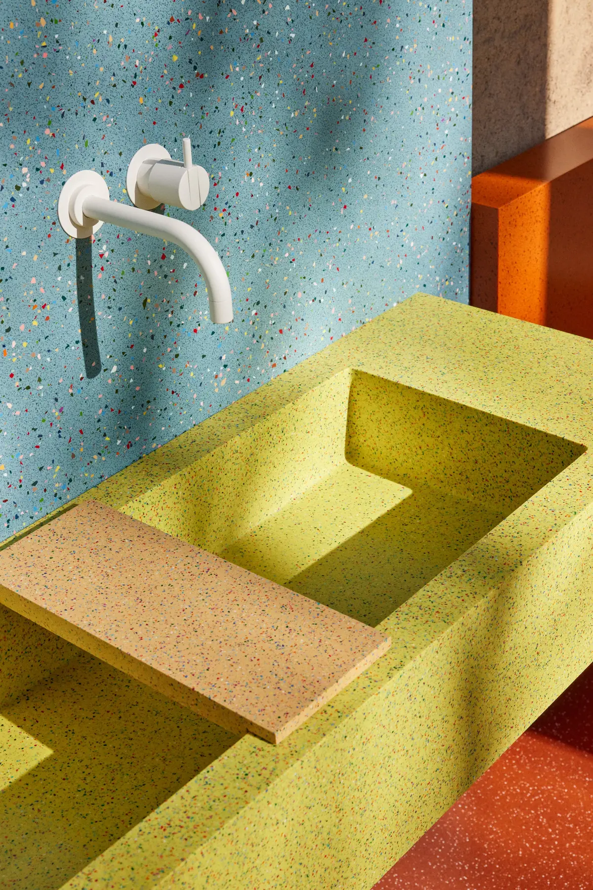Lavabo corrido verde lima con una tapa de color arena ante una pared azul moteada con grifería blanca