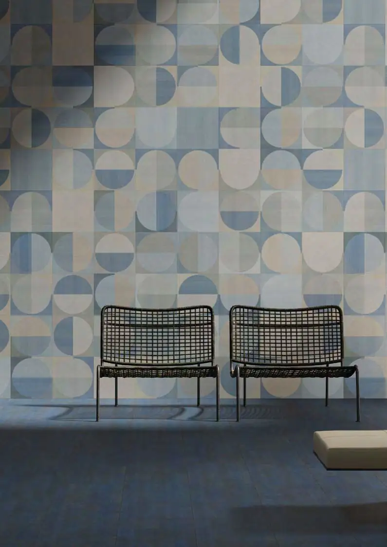 Pared con motivo geométrico de círculos y semicírculos en azules y beige, con dos sillas de rejilla negras sobre un suelo azul
